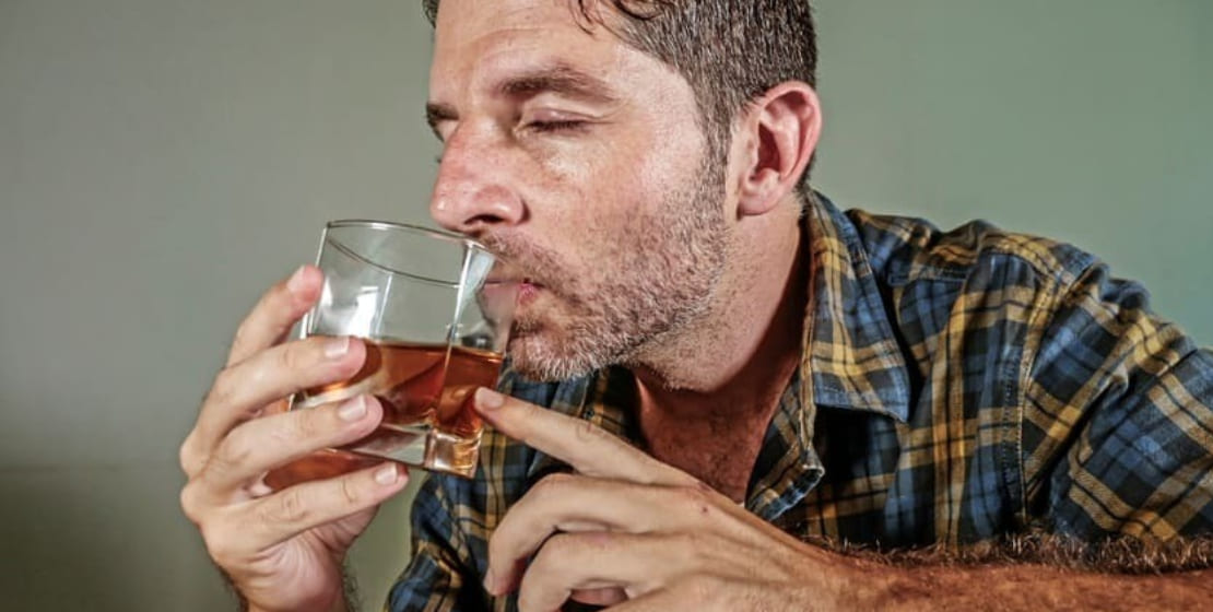 Мужчина пьет алкоголь из стакана